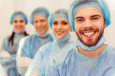 Beautiful doctors are looking at camera and smiling, standing in line in a modern operating roomの写真素材