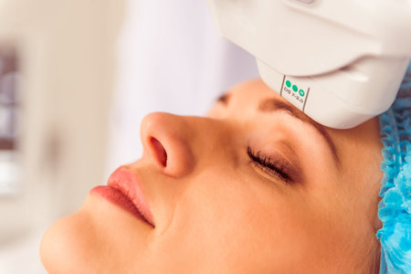 Beautiful female patient is getting a treatment while lying at cosmeticians office, close up