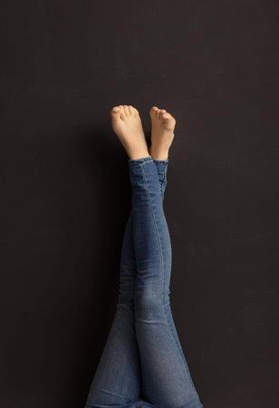 Beautiful slim crossed legs of young girl in jeans against dark background