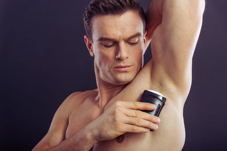 Portrait of handsome man using an antiperspirant, on a dark background