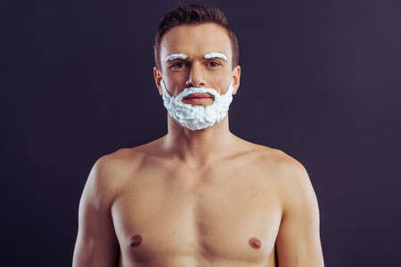 Portrait of handsome man with shaving foam on his face looking at camera and smiling, on a dark backgroundの写真素材