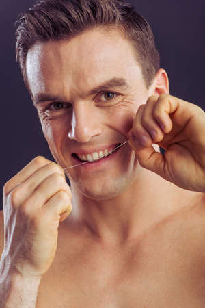 Portrait of handsome man using dental floss, looking at camera and smiling, on a dark backgroundの写真素材
