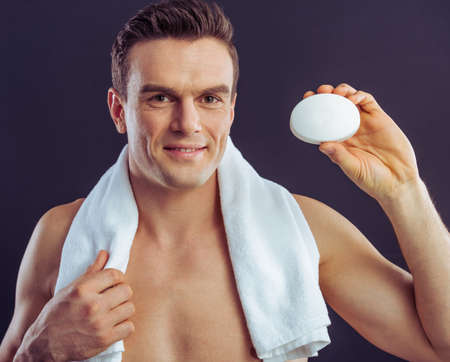 Portrait of handsome man holding a soap, looking at camera and smiling, on a dark backgroundの写真素材