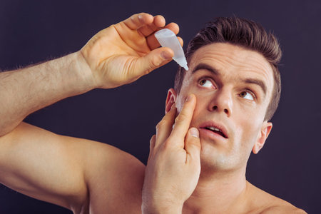 Portrait of handsome man instilling eye drops, on a dark backgroundの写真素材