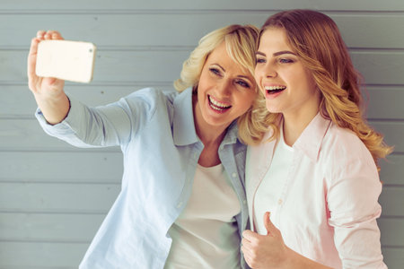 Portrait of beautiful mature mother and her daughter making a selfie using smart phone and smiling,...