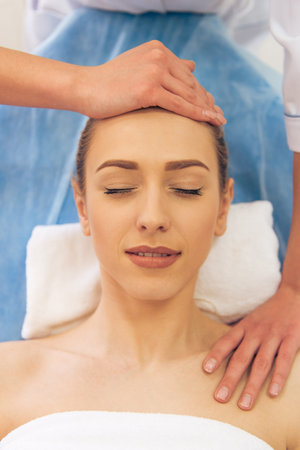 Top view of beautiful young woman getting a face massage, lying with closed eyesの写真素材