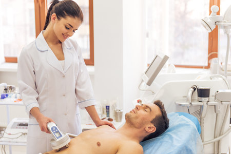 Handsome man is getting skin treatment. Female doctor is undertaking the procedure using a modern...