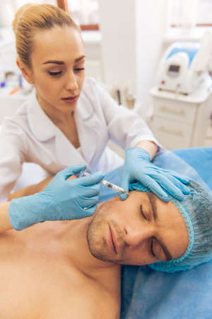 Handsome young man is getting an injection in face, a female doctor is giving an injectionの写真素材
