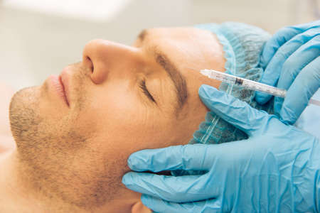 Side view of handsome young man getting an injection in face, lying with closed eyes, close-upの写真素材