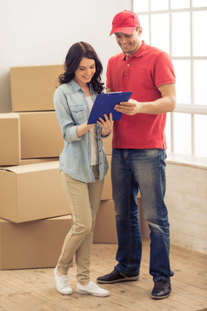 Attractive young woman and handsome delivery worker are signing documents for moving, cardboard...