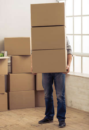 Handsome young man is moving, holding a cardboard boxes that covering himの写真素材