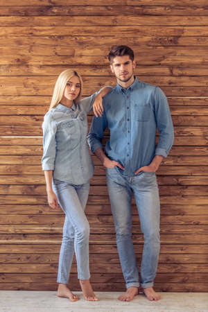 Full length portrait of beautiful young couple in jeans clothes looking at camera, standing against wooden wallの写真素材