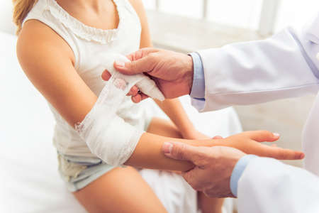 Handsome middle aged pediatrician is putting a bandage on little girl arm, close-upの写真素材