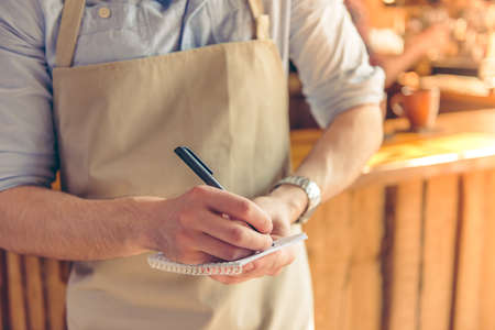 Cropped image of handsome young waiter making notes while taking an order, standing in the cafeの写真素材