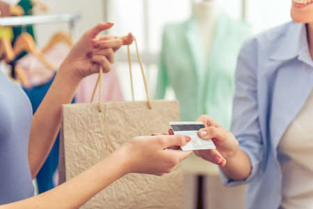 Cropped image of attractive young woman buying clothes in beautiful young designer using a credit card, standing in dressmaking studioの写真素材