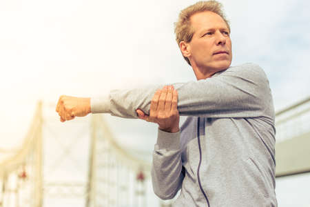 Handsome middle aged man in sports uniform is looking away and warming up during morning runの写真素材