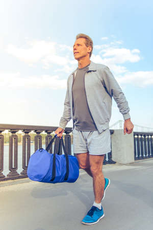 Handsome middle aged man in sports uniform is going with sport bag in his handの写真素材