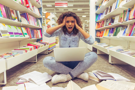 Beautiful Afro American girl is having stress while using a laptop and keeping hands on head,...