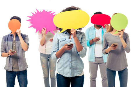 Young people of different nationalities are hiding faces behind speech bubbles while using smartphones, isolated on white backgroundの写真素材