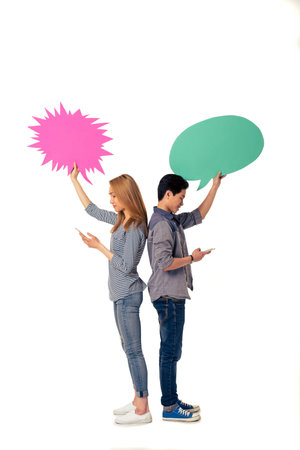 Attractive young Asian woman and man with speech bubbles are using phones and smiling, standing back...