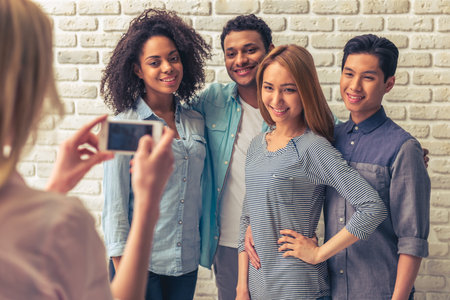Beautiful young people of different nationalities are smiling and posing, while girl is taking photoの写真素材