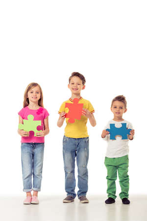 Full length portrait of cute little kids in casual clothes holding colorful puzzles, looking at camera and smiling, isolated on a white backgroundの写真素材