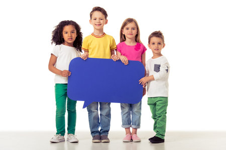 Full length portrait of cute little kids in casual clothes holding blue speech bubble, looking at camera and smiling, isolated on a white backgroundの写真素材