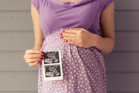 Cropped image of beautiful pregnant woman holding sonogram and keeping one hand on a belly