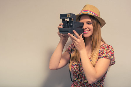 Attractive girl in summer clothes is using a camera and smiling, against gray background