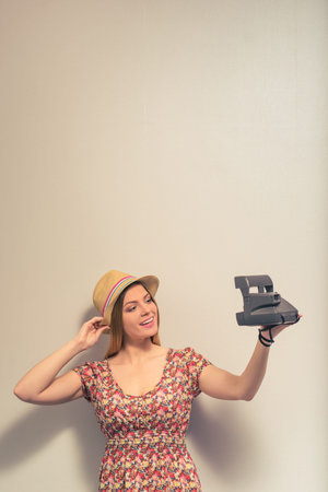 Attractive girl in summer clothes is making selfie using a camera and smiling, against gray backgroundの写真素材