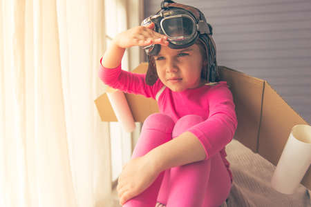 Cute little girl dressed like a pilot with toy wings is looking away while playing at homeの写真素材