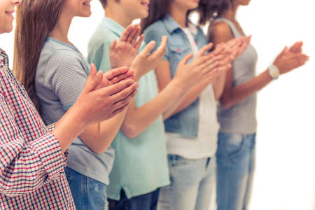 Cropped image of group of teenage boys and girls clapping hands, standing in a row, isolated on whiteの写真素材