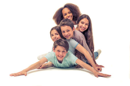 Group of teenage boys and girls is looking at camera and smiling while lying one on the other, isolated on whiteの写真素材