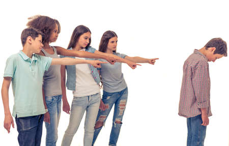 Group of teenage boys and girls is pointing on another boy, who is standing with bent head, isolated on whiteの写真素材