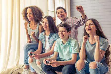 Group of teenage boys and girls is playing game console and smiling while sitting on the couch at homeの写真素材
