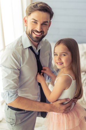 Cute little daughter is adjusting her father's tie. Both are looking at camera and smilingの写真素材