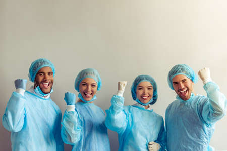 Surgeons of different nationalities and genders in medical wear are ready for the operation, showing fists, looking at camera and smilingの写真素材