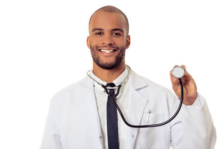 Portrait of handsome Afro American doctor in white coat looking at camera and smiling while holding a stethoscope, isolated on white backgroundの写真素材
