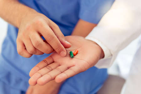 One doctor is taking pills from another doctor's palm, close-upの写真素材