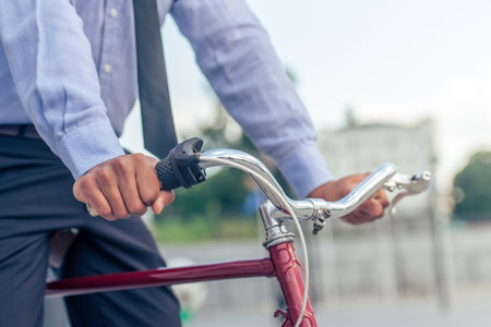 Cropped image of handsome Afro American businessman in classic clothes riding his bike