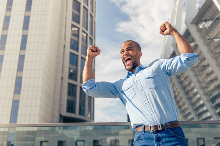 Low angle view of handsome young Afro American businessman keeping fists up and screaming with...