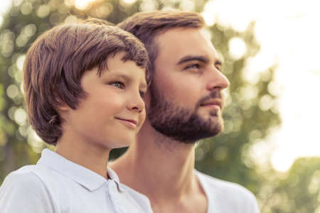 Portrait of handsome young dad and his cute little son looking forward and smiling while resting outdoorsの写真素材