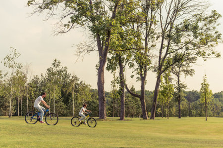 Panorama view of young dad and his little son in casual clothes riding bikes in parkの写真素材
