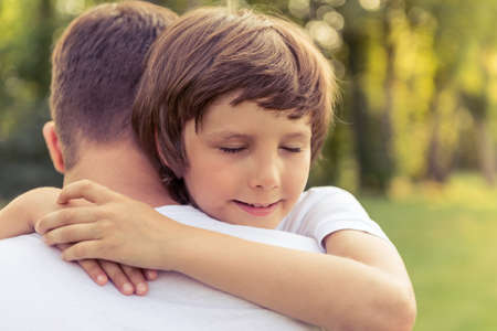 Portrait of cute little boy hugging his father while resting outdoorsの写真素材