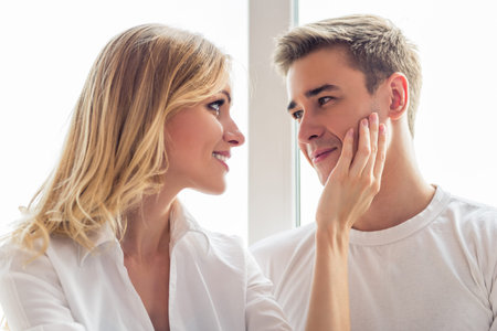Portrait of beautiful young couple in casual clothes looking at each other and smiling, sitting...
