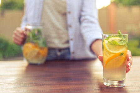 Cropped image of young girl is holding a glass of lemonade while standing outdoors. Glass in focusの写真素材