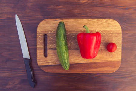 Top view of fresh vegetables, cutting board and knife on wooden tableの写真素材