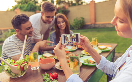 Young people are having picnic outdoors. Beautiful girl is taking photo of her friends using a...