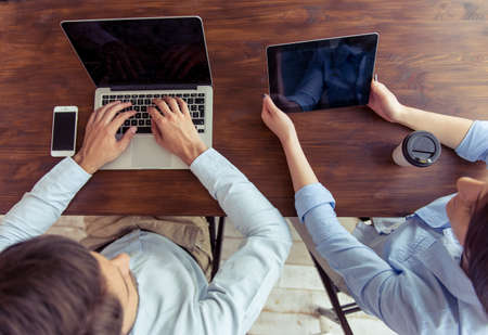 Top view of young business woman and businessman using gadgets and discussing affairs while working in officeの写真素材