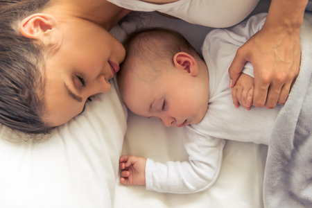 Top view of beautiful young mom and her cute little baby sleeping in bed at home, close-upの写真素材